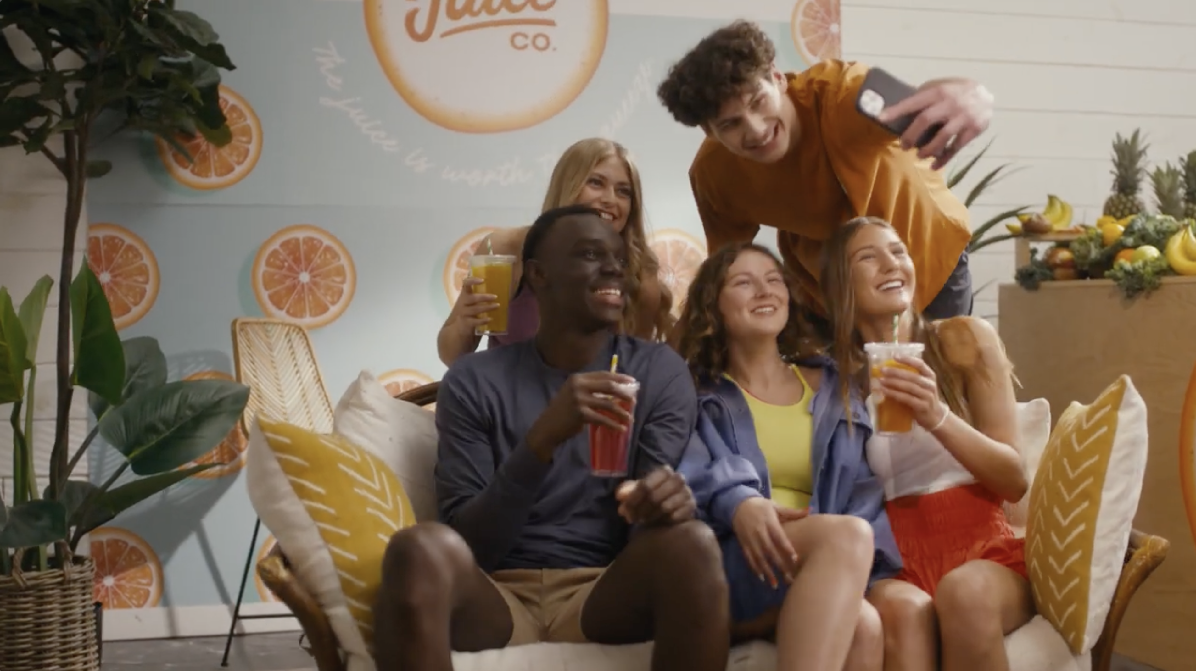 Five young adults sit together on a couch with drinks and take a group photo
