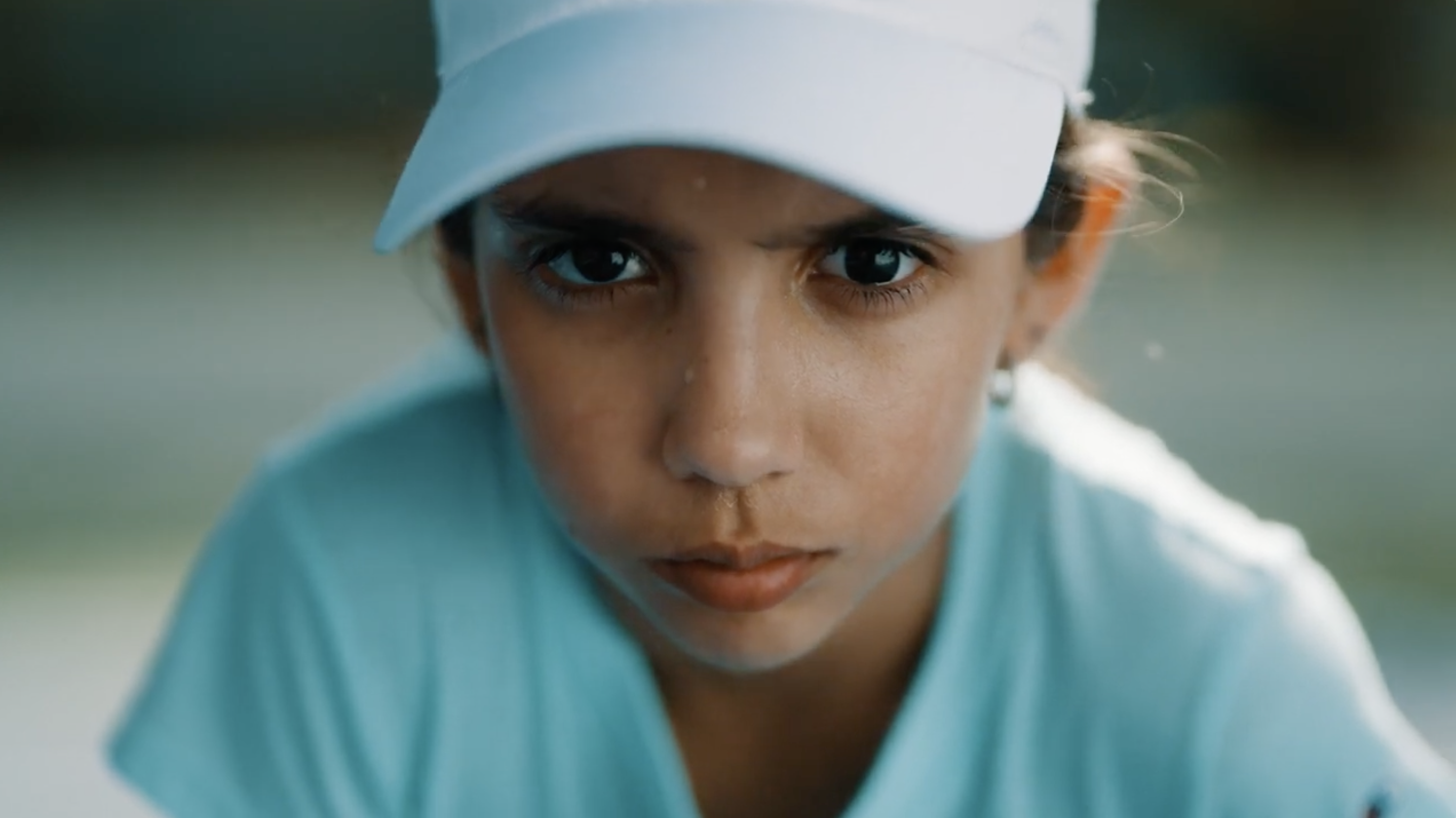 A young girl in a ball cap stares into the camera with an intense gaze