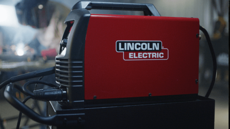 A Lincoln Electric LE31MP is in the foreground with a welder working in the background